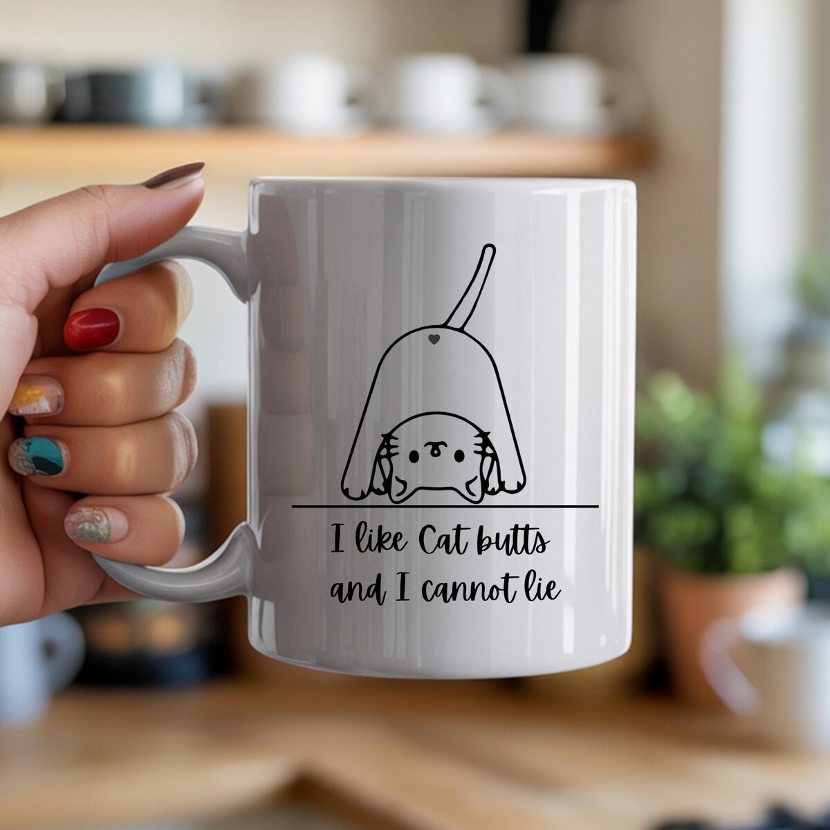 A white ceramic mug held in hand featuring a cartoon cat from behind with tail held high and the text I like cat butts and I cannot lie